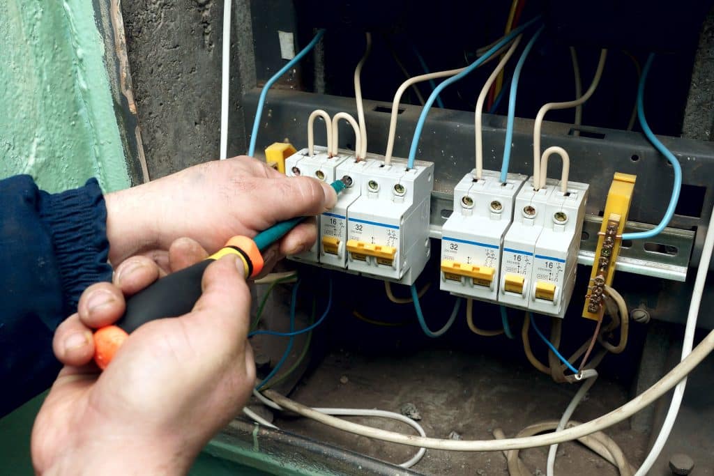 Electrician using a screwdriver to install and connect circuit breakers and wiring inside an electrical panel.